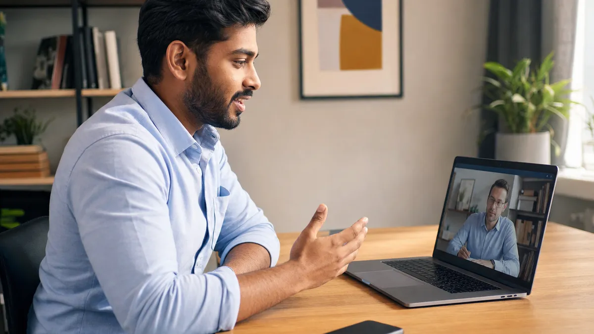 Candidata em um laptop durante uma entrevista por vídeo, gesticulando enquanto fala, com um celular apoiado com a tela para baixo na mesa ao lado