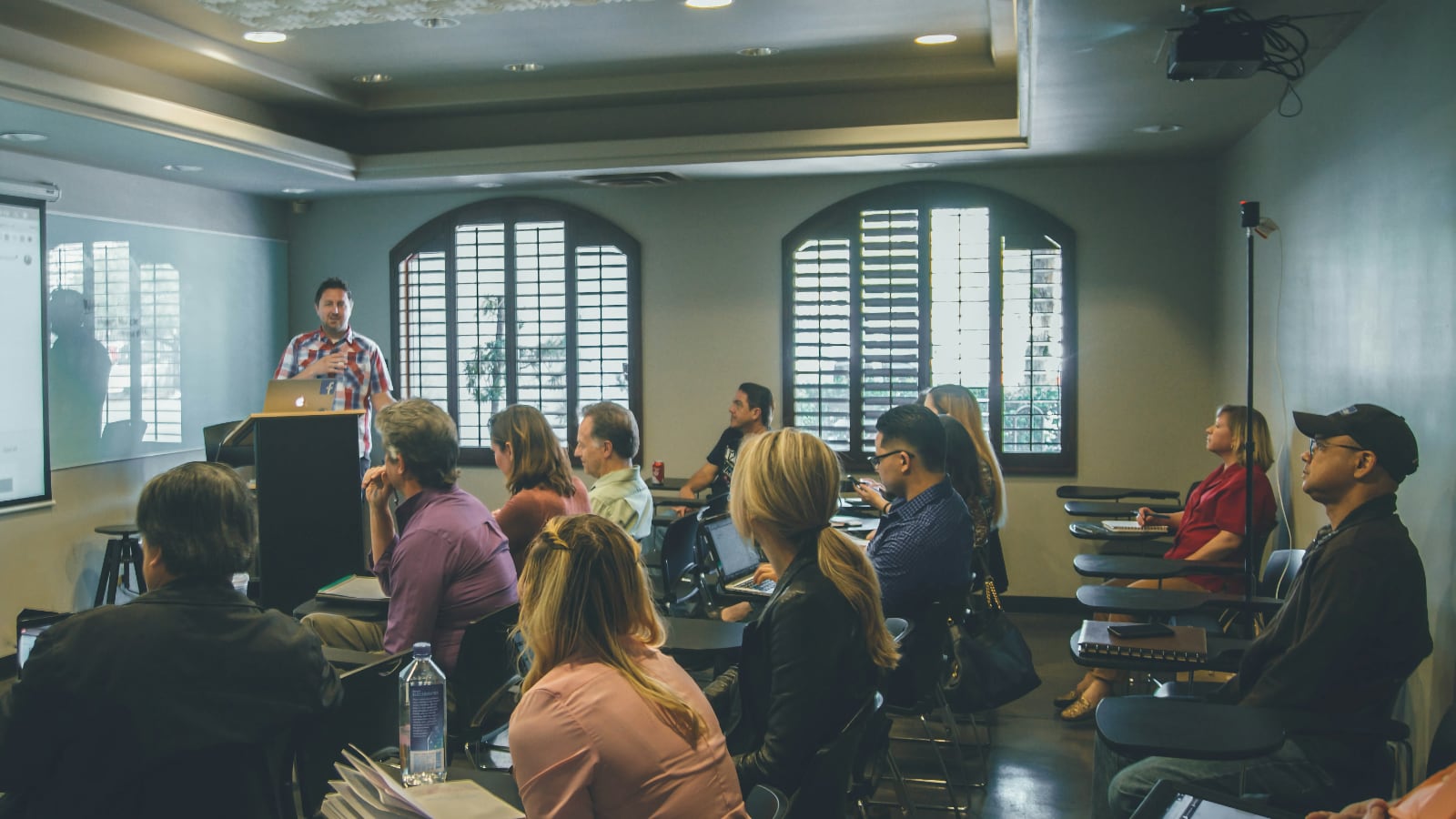 Orateur présentant devant un public assis dans une salle avec des fenêtres en arche